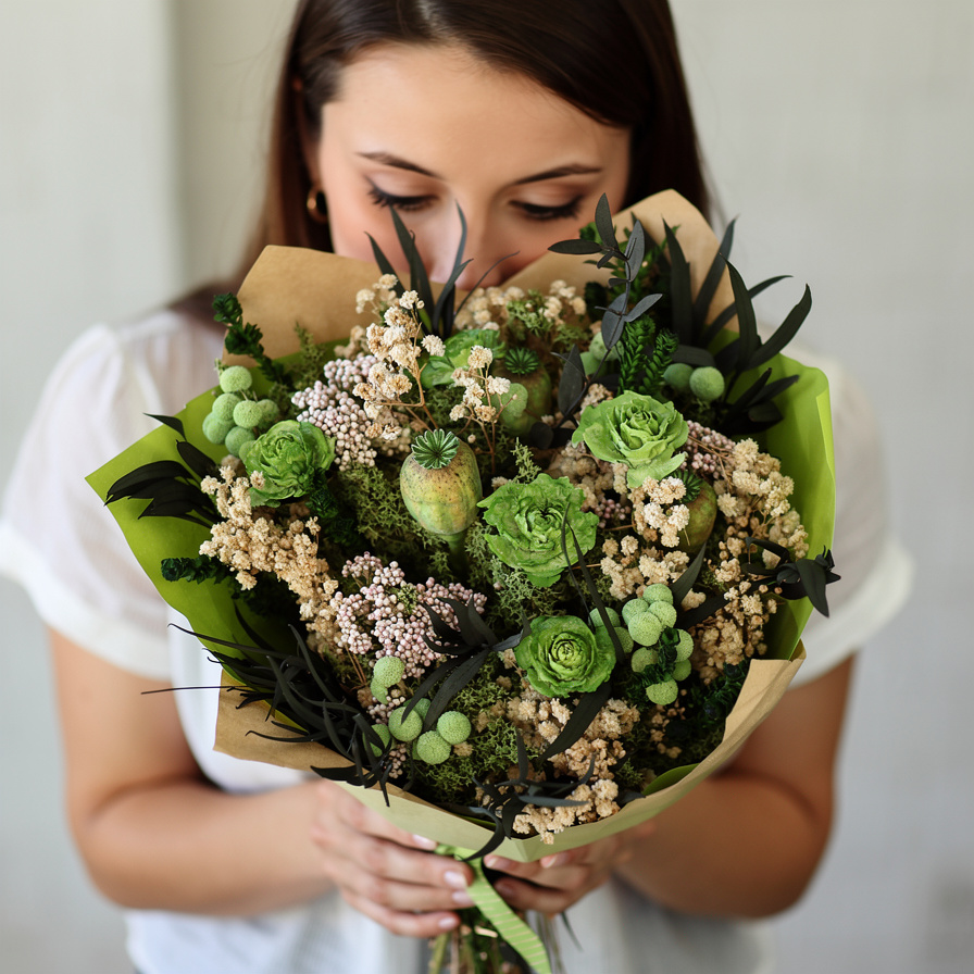 Ramo redondo de flores preservadas con rosas verdes, craspedia beige, eucalipto oscuro y envoltorio kraft, sobre fondo gris neutro. Estilo decorativo natural y silvestre.
